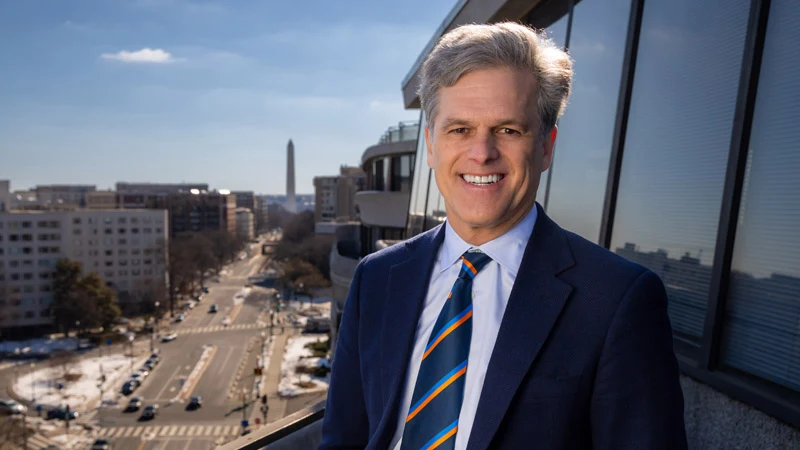 Timothy Shriver, 2026 Laetare Medalist, smiles in a blue suit with a striped tie, arms crossed.